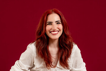 Confident woman looking at the camera and smiling while posing against a red isolated background.