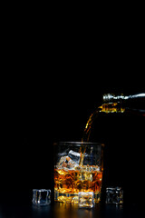 Pouring alcohol into glass, black background