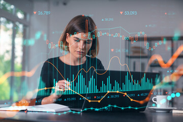 Pensive attractive beautiful businesswoman in formal wear working on laptop at office workplace in background. Forex graph and charts hologram icons. Concept of market trading and research.