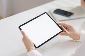 From a rear view, a businessman is seen holding and using a white screen digital tablet computer while sitting at his home office desk.