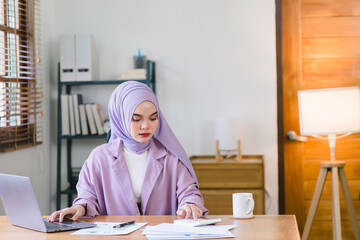 stunning Asian Muslim millennial businesswoman donning a purple hijab is seen working from her home office.