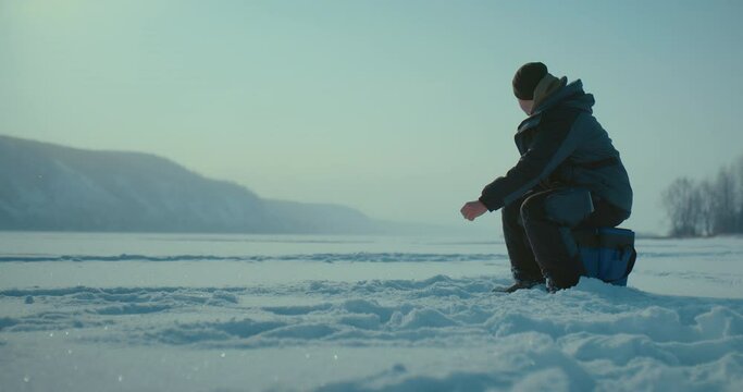 catching fish in iced river, fisher is putting down rod in ice hole, beautiful landscape, 4K, Prores