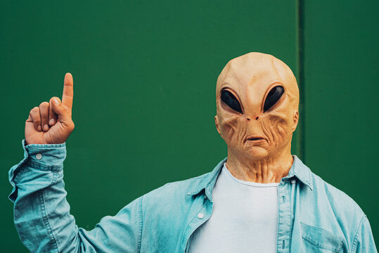 Portrait of alien mask man against a green wall background for copy text and write your text. Image concept for store sales discount offer with person pointing finger hand and looking on camera