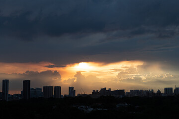 Warm sunset after rain with dark clouds above and silhouette of tall buildings and houses in foreground