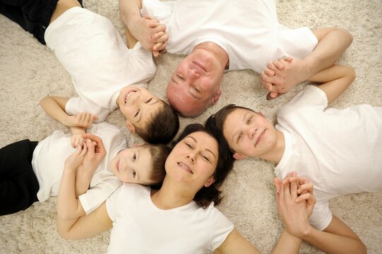 Happy family concept. Top view happy family five tied to each other and smiling, lying on a wooden floor with a carpet. Caucasian large family in the living room on a warm floor. High quality photo
