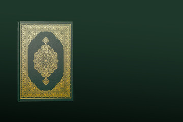 The Holy Al Quran with written arabic calligraphy meaning of Al Quran and rosary beads or tasbih on dark green black background with copy space.