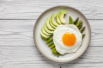 Tasty breakfast. Fried eggs with green asparagus and avocado on the plate on wooden table. Top view