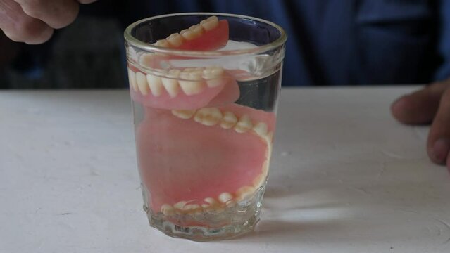 close-up in a glass of water, a pensioner puts removable dentures, hygiene and care for dentures, implantation of teeth, restoration of chewing function, be healthy