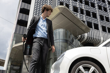 Below view of progressive businessman with electric car recharging at public charging station at...