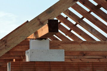Wooden rafters and a wall plate, walls made of autoclaved aerated concrete blocks, a reinforced concrete beam, blue sky in the background