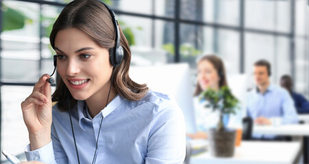 Fototapeta premium Female customer support operator with headset and smiling, with collegues at background.
