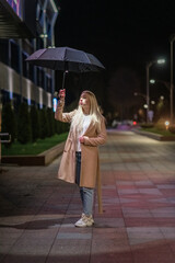 Portrait of a young beautiful fair-haired girl in a coat and with an umbrella in the night city.