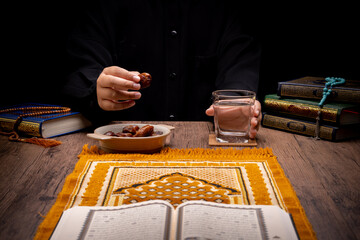 Many Date Palms are on bowls, plates, and cups of water, and the Quran is on wooden tables, to wait for the time of Iftar, with the concept of ramadan Muslims, Arabic calligraphy meaning of Al Quran