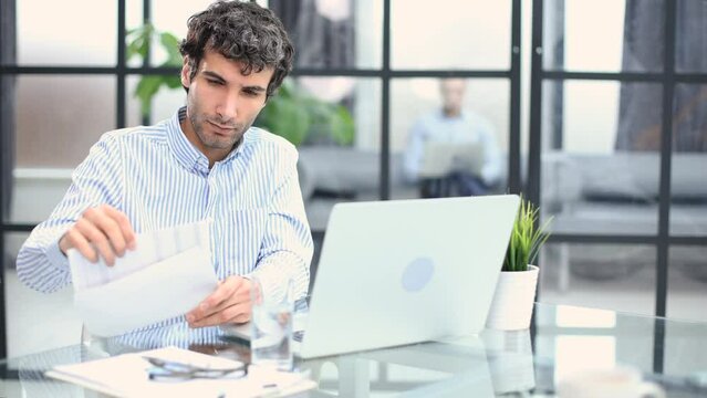 Entrepreneur opening an envelope in a desktop at office. Collegue is on the background.