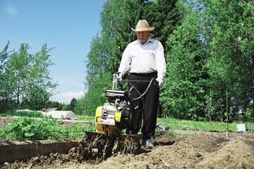 Obraz premium The farmer is digging a garden. The harvester plows the garden. The gray-haired grandfather mows the garden.