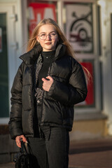 Portrait of a young beautiful blonde girl in glasses on a spring sunny day in an urban environment.