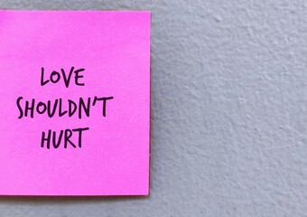 Pink note stick on grey background with handwritten LOVE SHOULD NOT HURT, means everyone deserves to be safe in relationship, should not be hurt by partner  physically, emotionally, or sexually