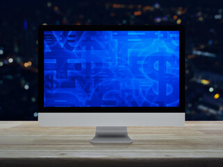 Financial currency symbol on desktop computer monitor screen on wooden table over blur colorful night light city tower and skyscraper