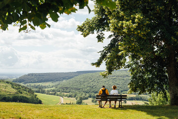 Un couple assis sur un banc admirant un paysage de Bourgogne. Des touristes sur un banc regardant le paysage. A l'ombre d'un arbre, un couple se repose face &agrave; un panorama.
