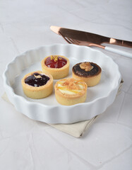 mini bake cute crisp creamtart with colourful flavour like chocolate coffee walnut, golden blueberry, strawberry osmanthus, mango vanilla in crystal plastic box on white marble pastry halal party menu