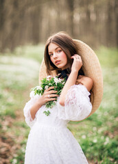 Portrait of a beautiful young brunette in a spring forest. A girl with a bouquet of primroses in her hands