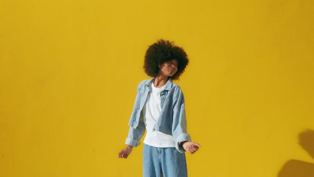 Playful happy young African American woman wear stylish denim clothes dancing and jumping funky black teen fashion girl on summer yellow background, horizontal banner header website design, copy space