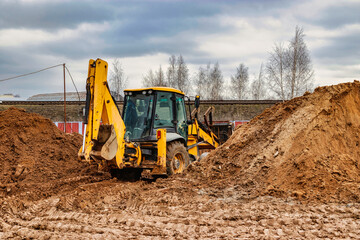 A universal excavator is working on a construction site against a cloudy sky. Earthworks at a construction site. Modern earthmoving equipment. The contractor is doing construction work.