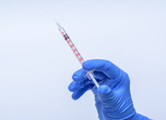 szczepionka - strzykawka trzymana w dłoni w niebieskiej rękawiczce na białym tle - obrazy, fototapety, plakaty
