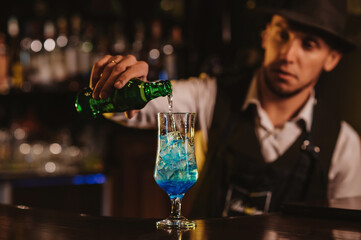 bartender mixes a blue lagoon cocktail in a glass with ice at bar counter in a restaurant