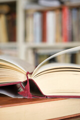 Open book or textbook on a pile of closed books in front of a bookcase in a library. Education learning concept. Image with selective focus.