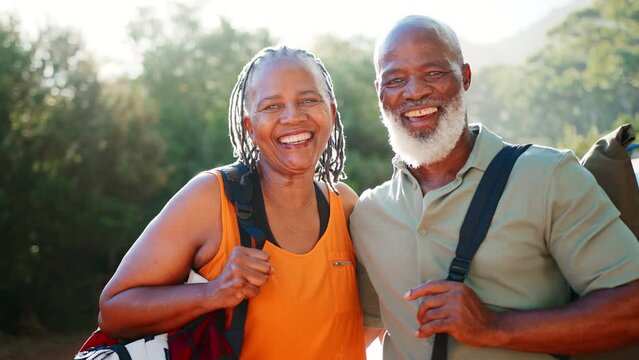 Portrait of smiling senior couple with backpacks going for hike in countryside standing by car together - shot in slow motion