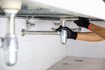 Technician plumber using a wrench to repair a water pipe under the sink. Concept of maintenance,...