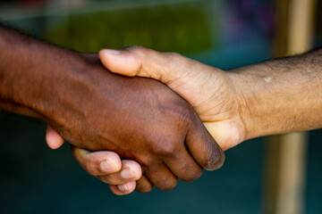 Tow friends are doing handship and one has black hands and the other has white hands