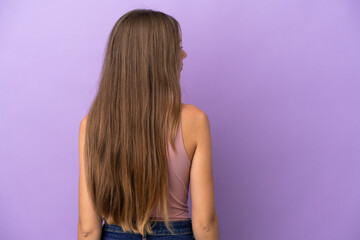 Young Lithuanian woman isolated on purple background in back position and looking side
