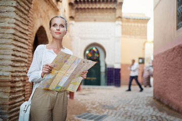 Travel and active lifestyle concept. Young traveller woman walking in ancient moroccan town holding...