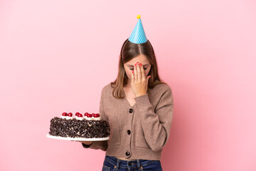 Young Lithuanian woman holding birthday cake isolated on pink background with tired and sick...