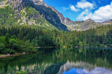 Fototapeta na wymiar Beautiful summer landscape of High Tatras, Slovakia - Poprad lake, lush forest, reflecting on water surface, mountains and white clouds on the sky