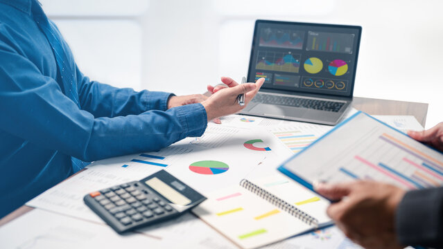 Businessman is pointing to financial report while brainstorming with developer collaborating on a successful plan for their upcoming project, as they work together on necessary paperwork and planning.
