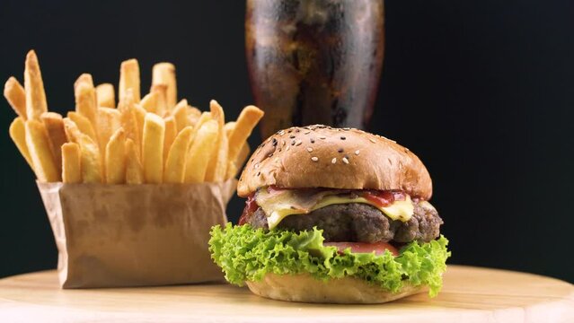 Beef burger with crispy french fries and cold cola on wooden rotating plate