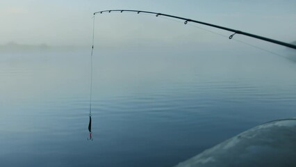 The spinner swings in the wind while fishing from a boat in the morning on the lake