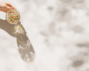Top view of wineglass in female hand, white wine with beautiful shadows and glare at sunlight,...