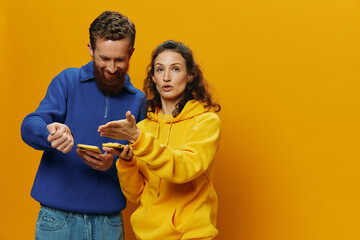 Woman man cheerful couple with phones in hand social networking and communication crooked smile fun and fight, in yellow background. The concept of real family relationships, freelancers, work online.