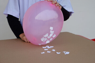 Closeup student do science experiment about static electricty from pink balloon and pieces of...