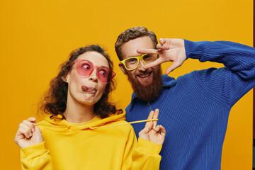 Man and woman couple smiling cheerfully and crooked with glasses, on yellow background, symbols...