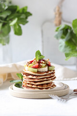 Stack of pancakes with strawberries, nuts, fruits and mint.