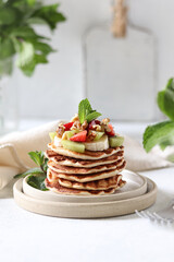 Stack of pancakes with strawberries, fruits, nuts and mint.