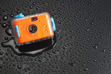 orange pocket camera or  film camera in waterproof case with water drop on black background with...