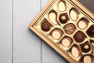 Partially empty box of chocolate candies on white wooden table, top view. Space for text