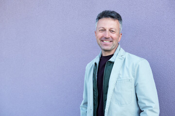 Middle-aged man posing over lilac wal. Handsome mature man. Outdoor male portrait.