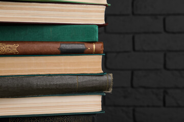 Many old hardcover books near black brick wall, closeup. Space for text